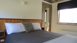 Un lit recouvert d’une couvre-lit sombre et orné de coussins à motifs, une tête de lit en bois, une petite table de chevet et une fenêtre donnant sur l’extérieur.