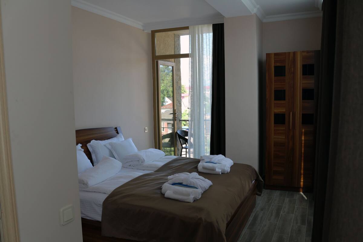 A hotel room with a large bed, a wooden wardrobe, and a view of the outdoors through a glass door.