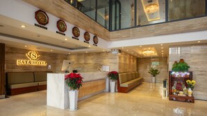 Eine Hotelhalle mit Empfangsschalter, Sitzgelegenheiten und dekorativen Elementen wie Uhren und Pflanzen.