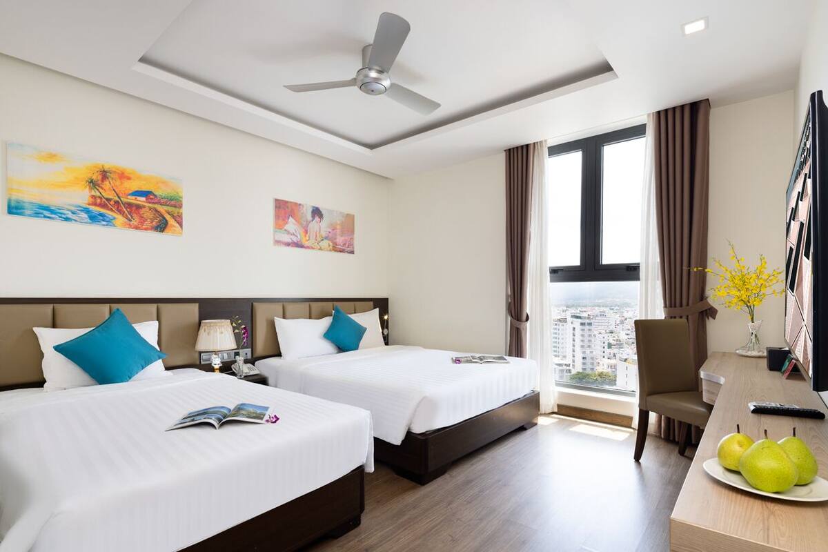 Une chambre d’hôtel avec deux lits, un bureau, une chaise, une télévision et une fenêtre donnant sur la ville.