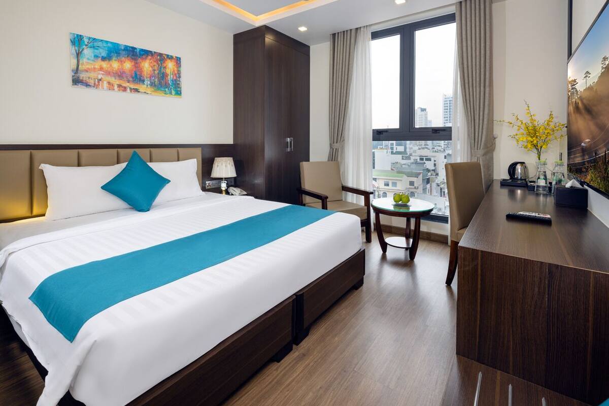Une chambre d’hôtel avec un grand lit, un bureau, une chaise et une vue sur la ville par la fenêtre.