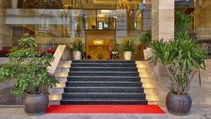 Eine Hotelhalle mit Marmorstufen, Kübelpflanzen und einem roten Teppich, der zum Eingang führt.