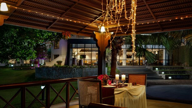 An outdoor dining area with a table set for two, string lights, and a view of the building in the background. - Vivanta Katra Vaishno Devi (Reasi)