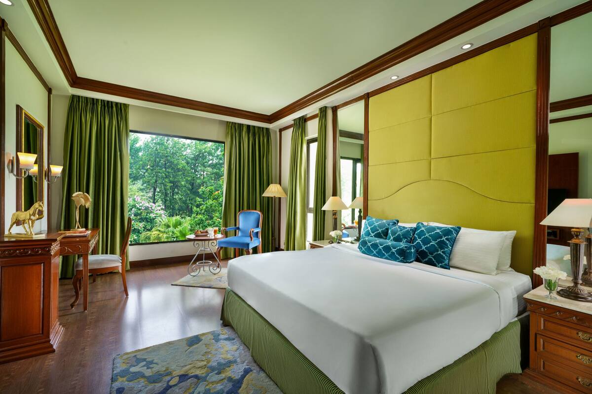 Habitación de hotel con una cama grande, un escritorio con silla, una mesita y vistas a zonas verdes.