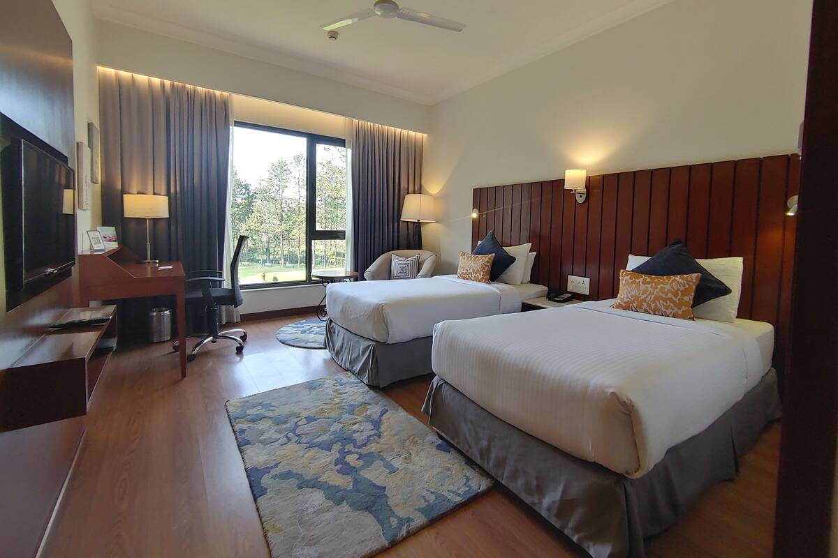 Habitación de hotel con dos camas, un escritorio, televisor y vistas al exterior.