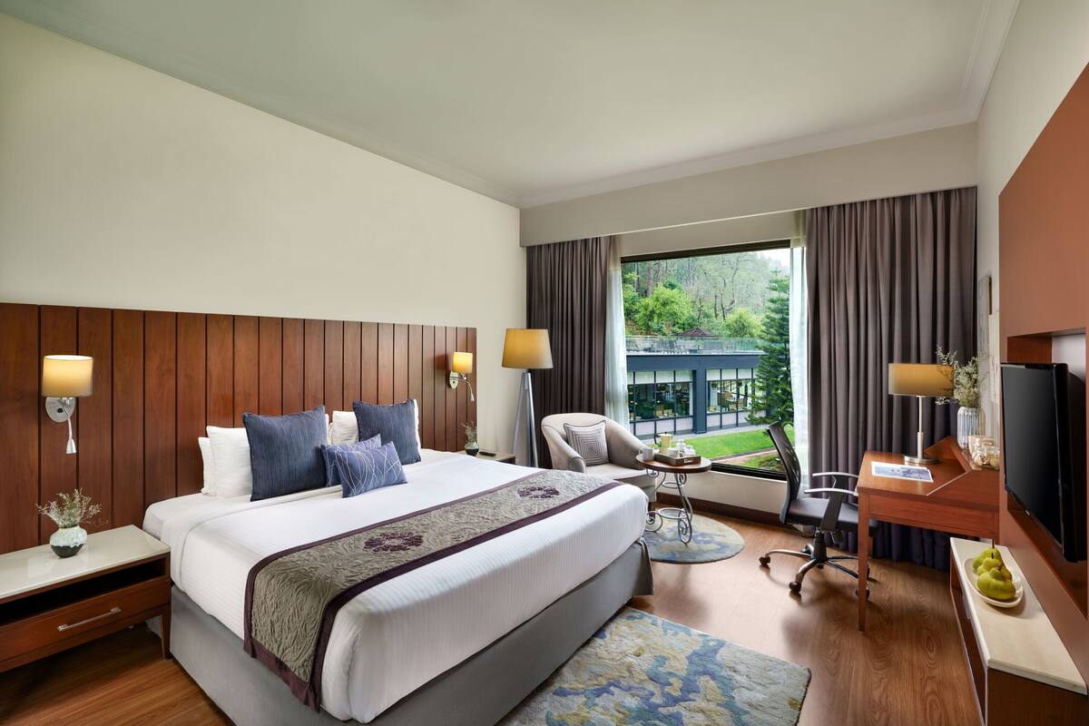Habitación de hotel con una cama grande, lámparas de noche, un escritorio con televisor y vistas al exterior.
