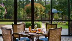 A dining table with wicker chairs, a glass of orange juice, a bottle of water, and plates of fruit and pastries. - Vivanta Katra Vaishno Devi (Reasi)
