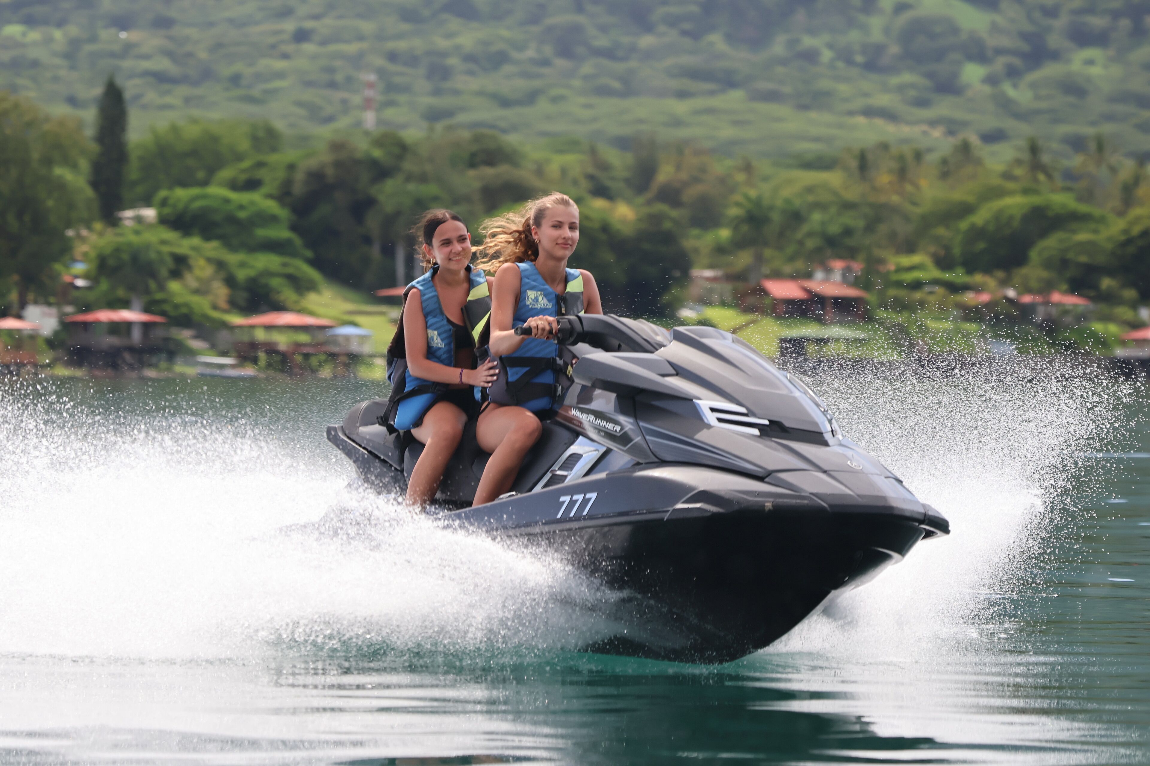 Two people on a jet ski with a number 777, surrounded by water and greenery.