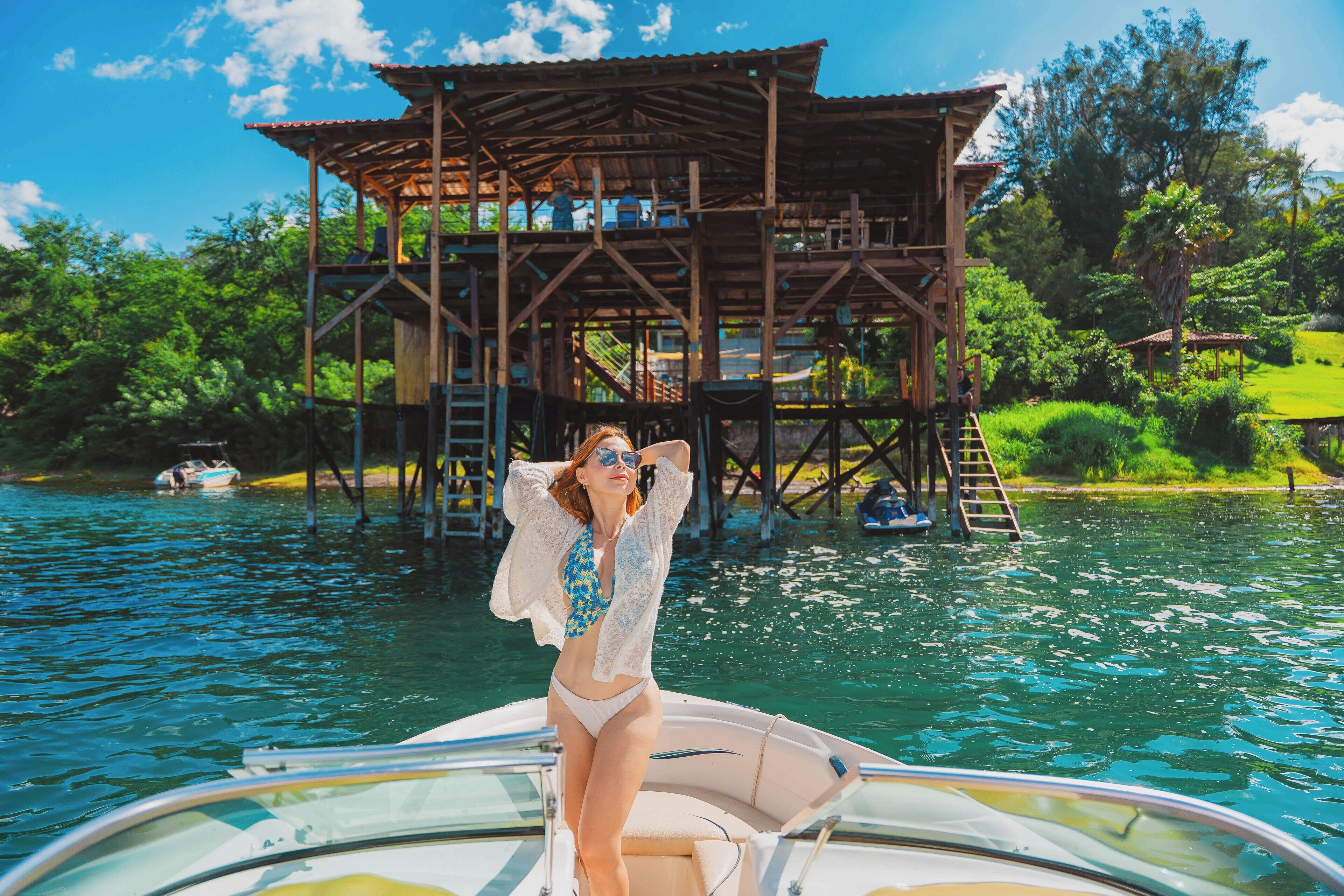 Une femme, vêtue d’un maillot de bain blanc et bleu, se trouve sur un bateau près d’une structure en bois dotée d’un toit.