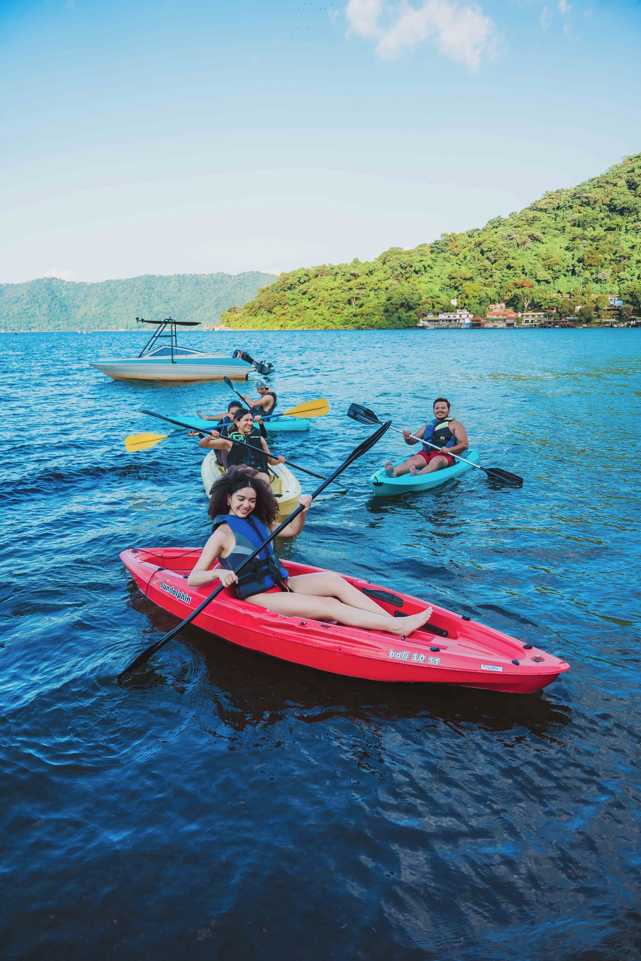 A group of people kayaking on a calm lake with a forested hillside in the background.