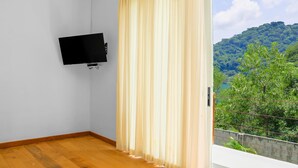 A room with a wooden floor, a mounted TV, and a window with curtains. - Equinoccio Hotel (Santa Ana)