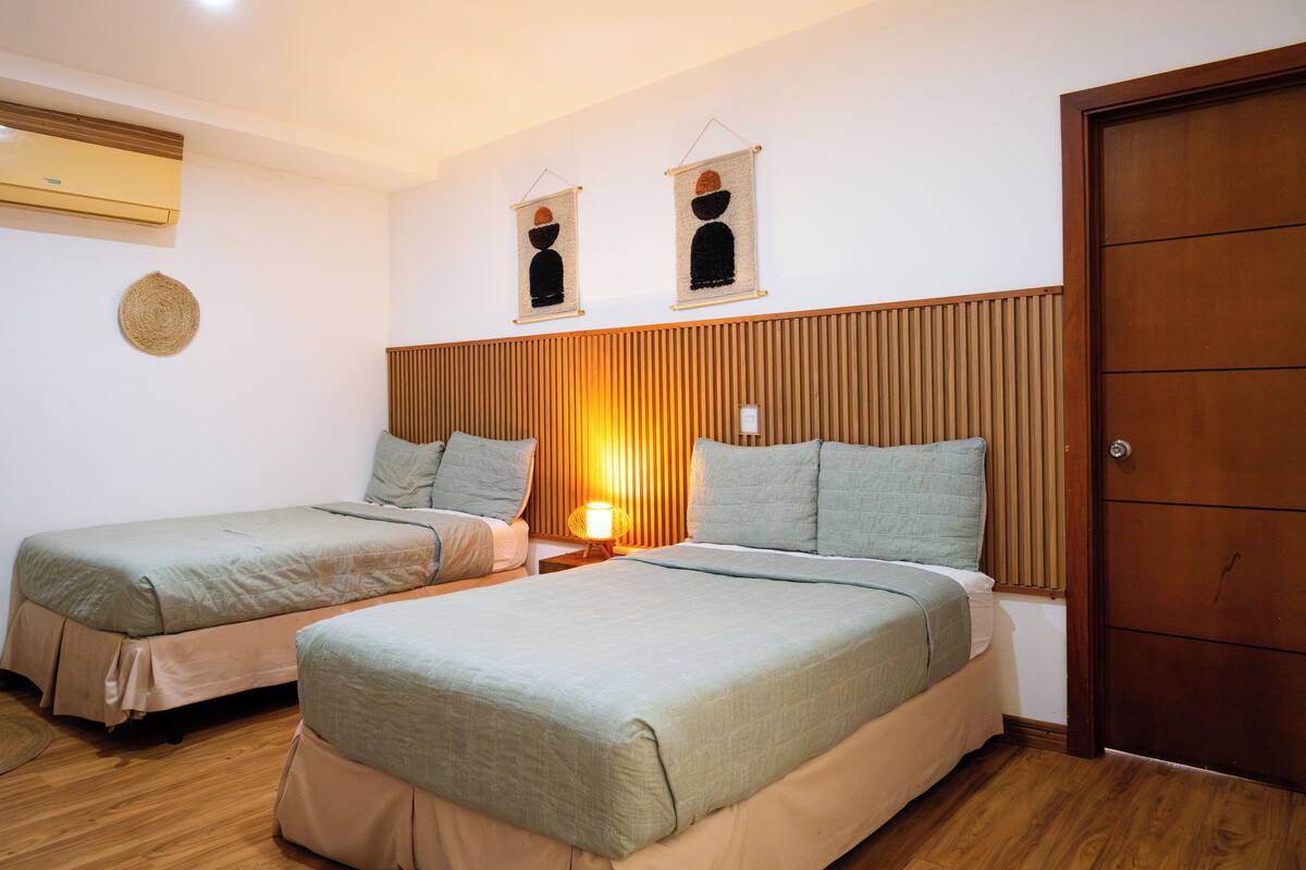 A hotel room with two single beds, a wooden headboard, a wall-mounted air conditioner, and a door.