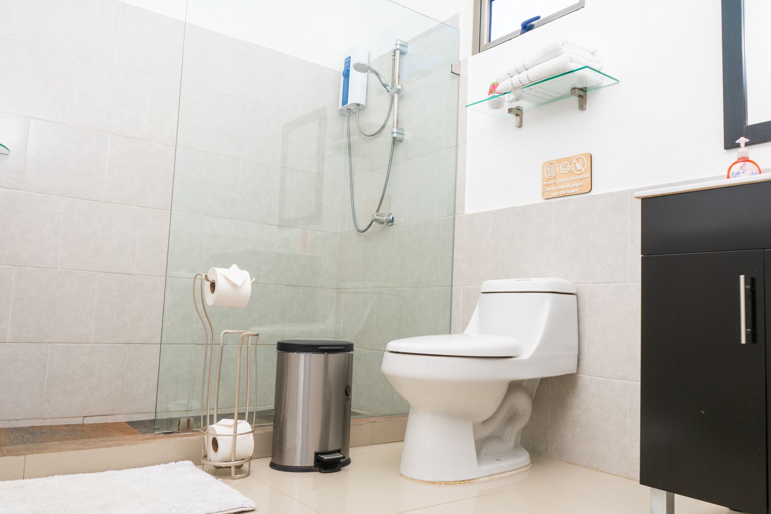 A modern bathroom with a toilet, a shower, a trash bin, and a towel rack.