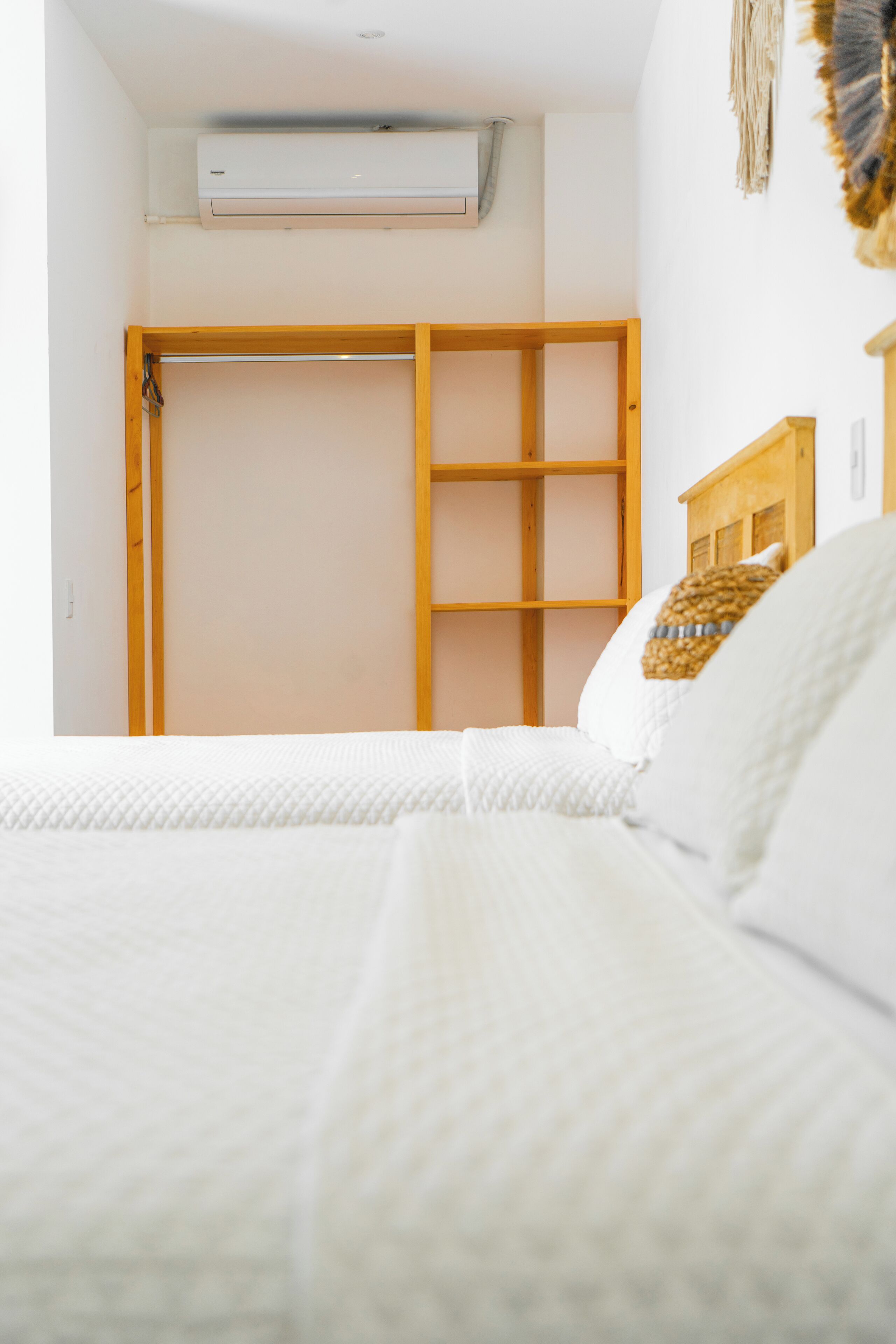 A bedroom with a bed, a wooden wardrobe, and an air conditioning unit on the wall.