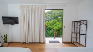 A room with two beds, a TV, a large window with curtains, and a view of greenery outside. - Equinoccio Hotel (Santa Ana)