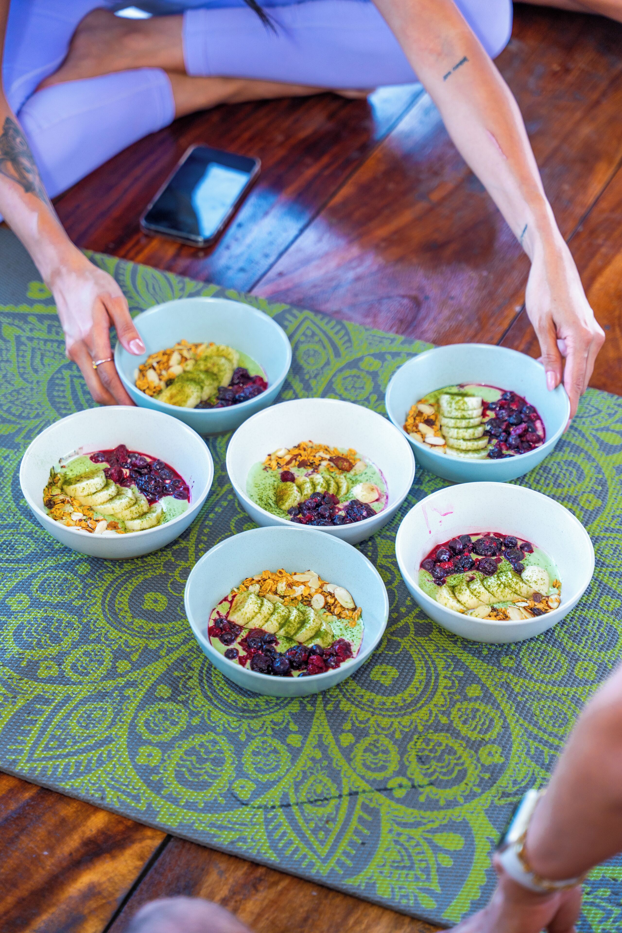 A person arranging bowls of food on a patterned mat.
