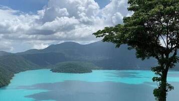 Vista panorámica de un lago turquesa rodeado de colinas verdes exuberantes y un cielo despejado.