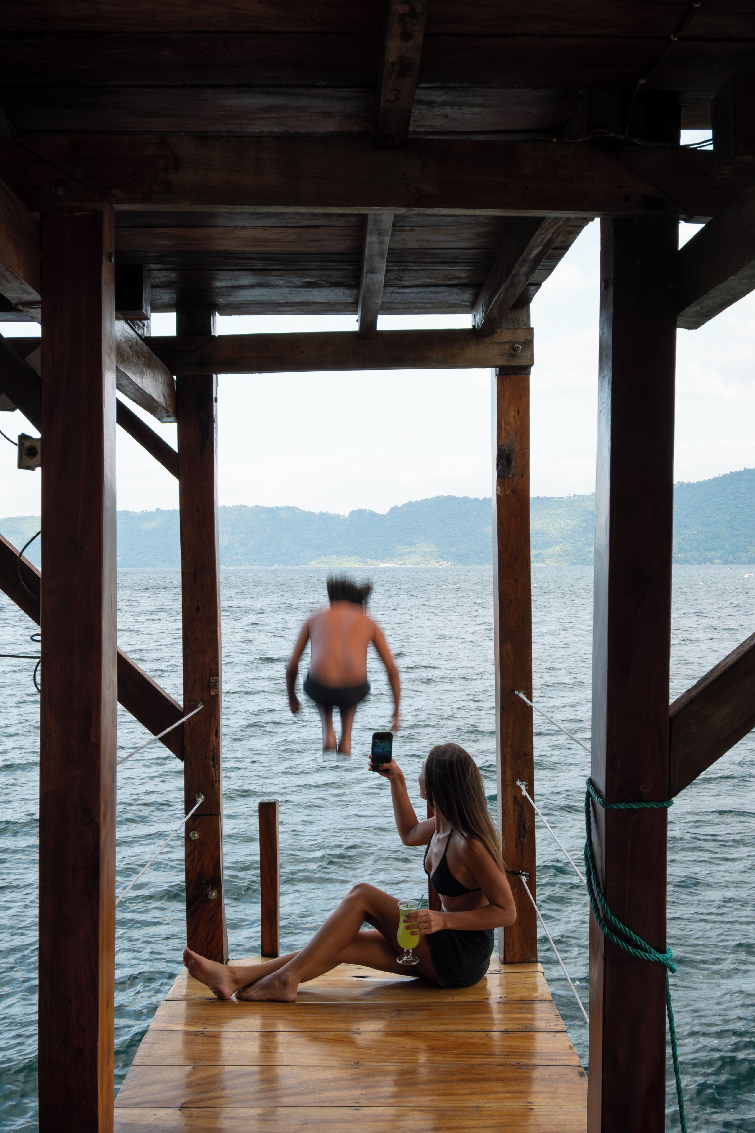 Une jetée en bois s’étendant au-dessus de l’eau, avec une personne assise et une autre personne debout, plus loin.