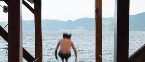 A wooden dock extending over water with a person sitting and another person standing in the distance.