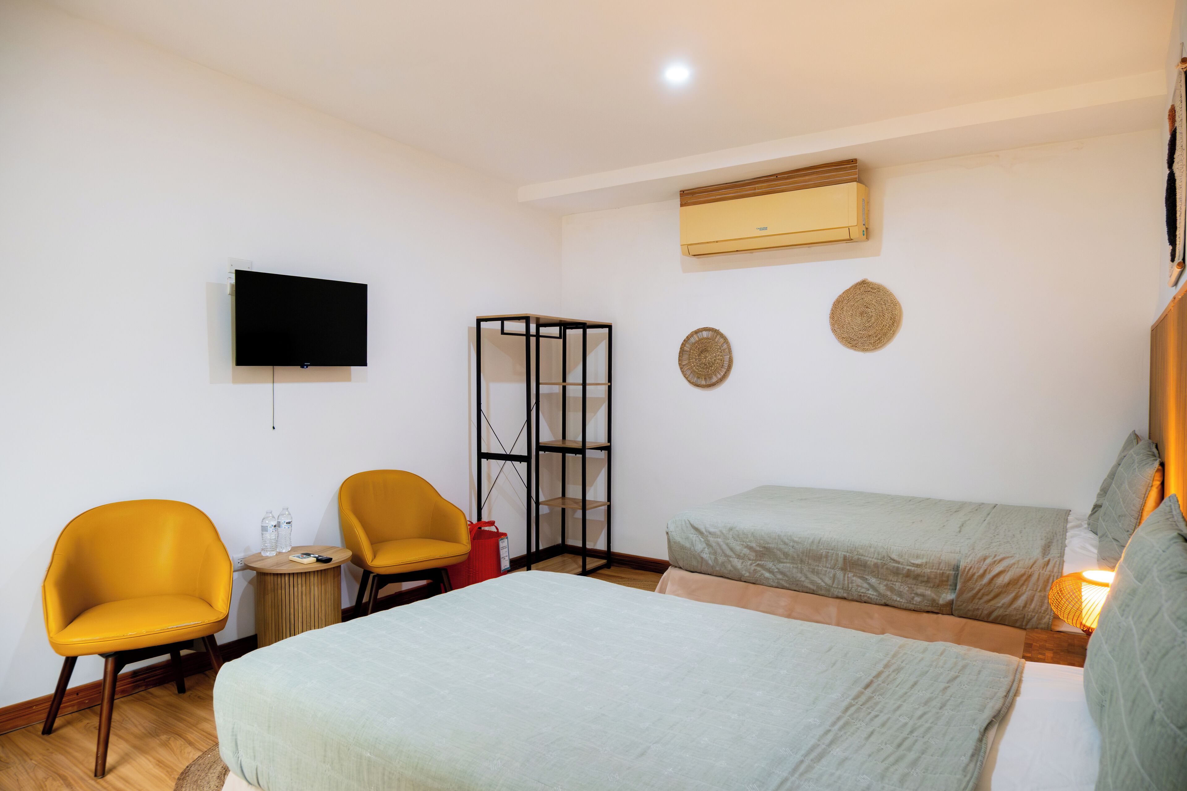 A hotel room with two beds, a TV, a small table with bottles, and a chair.
