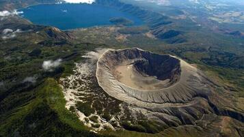 Vista aerea di un ampio cratere con un lago, circondato da terreno accidentato e vegetazione rada.