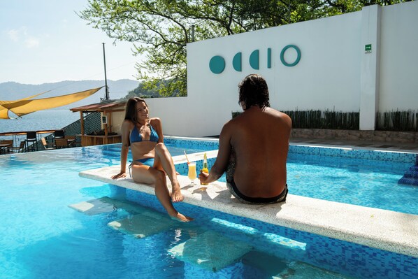 A pool area with a white wall, a wooden deck, and a view of the sea. - Equinoccio Hotel (Santa Ana)