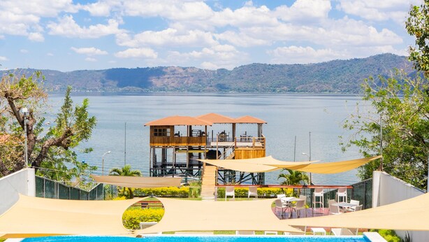 A swimming pool with lounge chairs and a wooden deck overlooking a lake. - Equinoccio Hotel (Santa Ana)