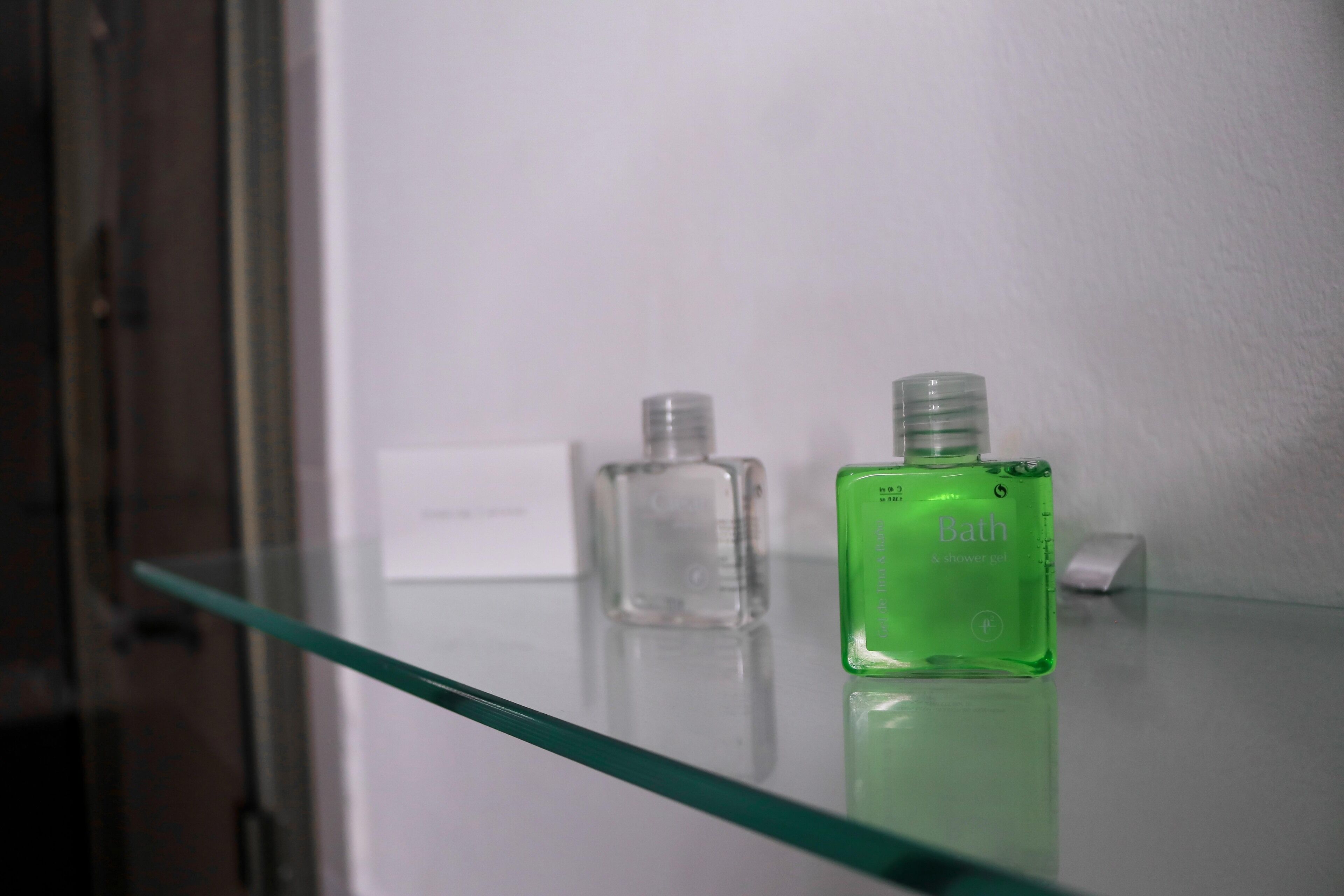 A glass shelf with two bottles, one green labeled "Bath" and one clear.