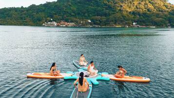 Eine Gruppe von Menschen sitzt auf Paddleboards auf einem ruhigen See, im Hintergrund ist ein bewaldeter Hügel zu sehen.