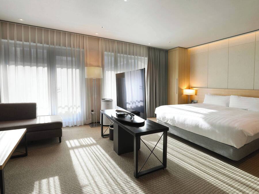 A hotel room with a bed, a desk, a television, and a sofa.
