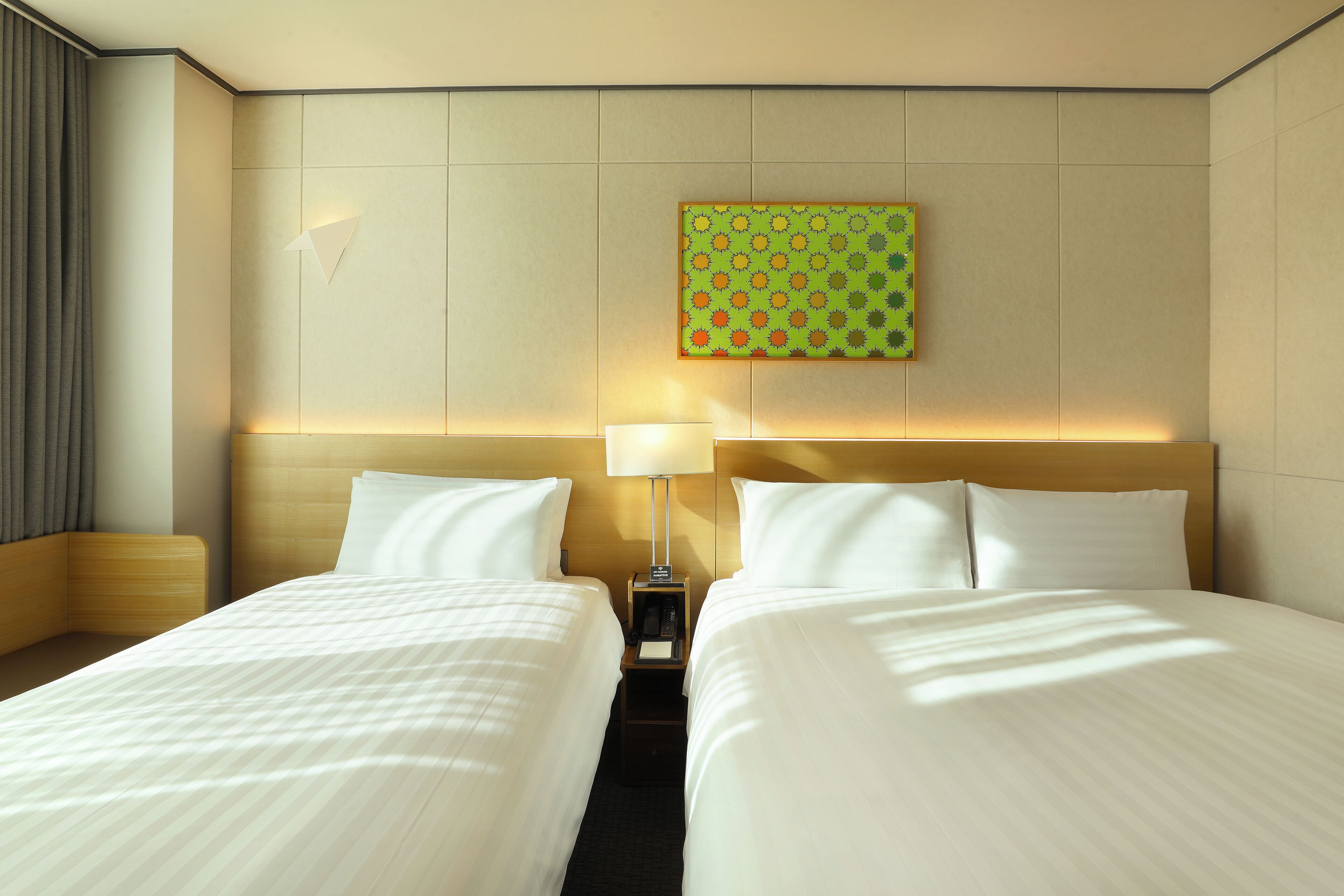 A hotel room with two beds, a nightstand, a lamp, and a wall-mounted artwork.