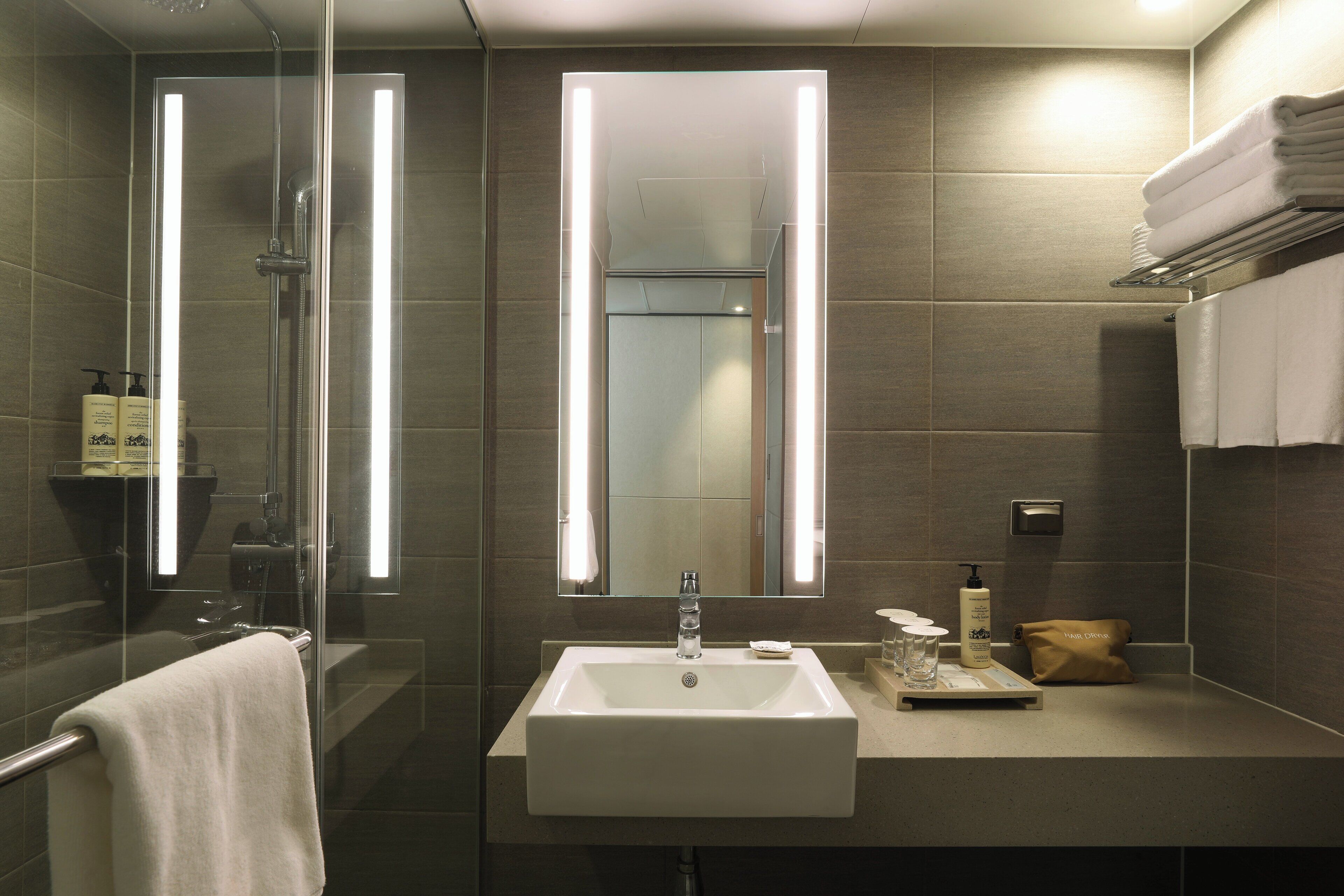Un baño moderno con ducha de vidrio, un lavabo blanco y un espejo encima.