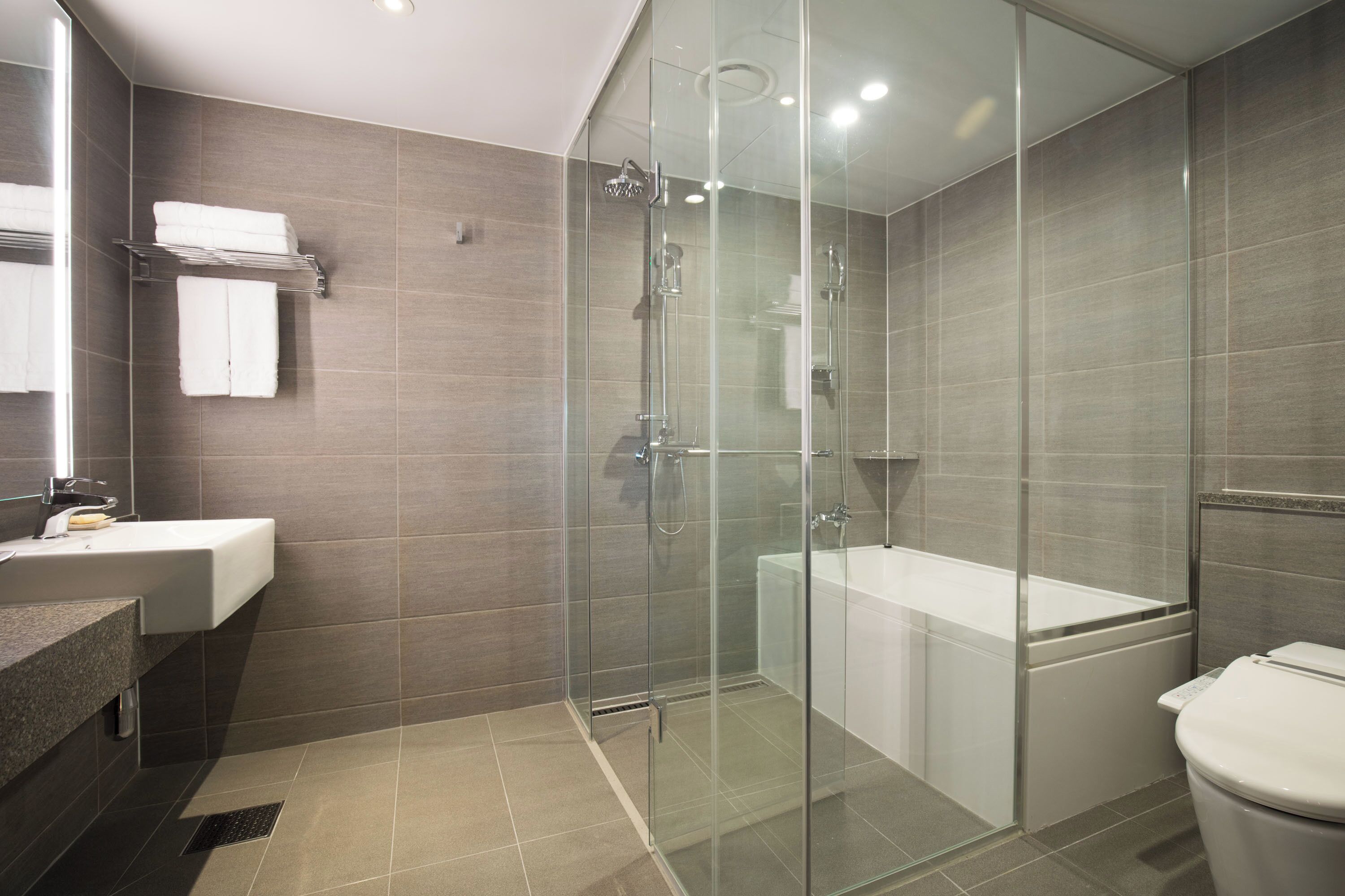 A modern bathroom with a glass-enclosed shower, a white bathtub, and a sink with a mirror.
