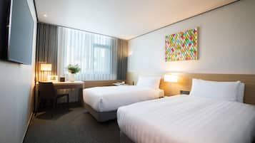 A hotel room with two beds, a desk, a chair, a TV, and a colorful artwork on the wall.