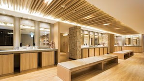 A modern bathroom with wooden benches, a stone accent wall, and multiple mirrors.