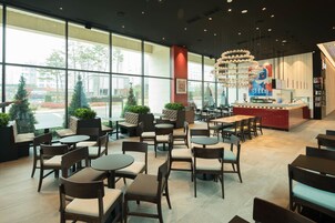 A spacious indoor seating area with multiple tables and chairs, large windows offering views of the outside, and a central counter with a sign.