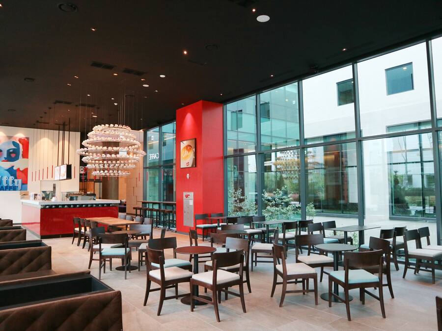 A modern restaurant interior with high ceilings, large windows, and a central chandelier.