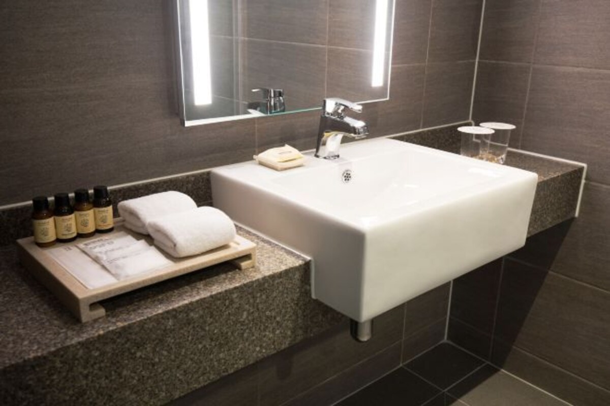 A modern bathroom with a rectangular white sink, a mirror above it, and a shelf with toiletries.