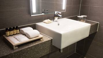 A modern bathroom with a white sink, a mirror above it, and a shelf with toiletries.