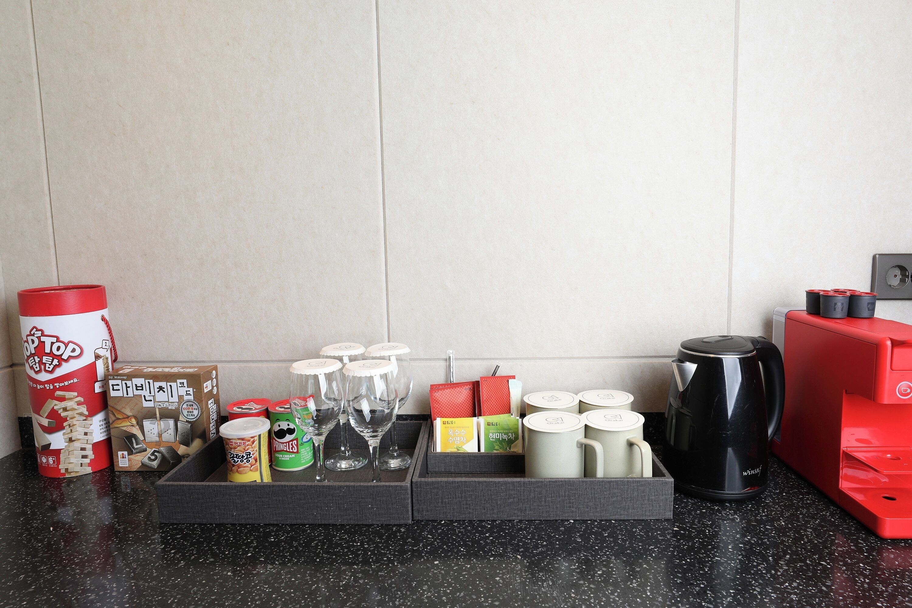Un taulell de cuina amb diversos objectes, com una cafetera, un aparell vermell i una caixa de llaminatures.