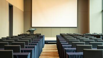A conference room with rows of tables and chairs, a podium, and a large projection screen.