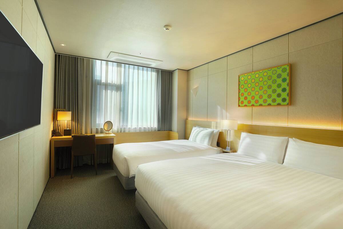 Une chambre d’hôtel avec deux lits, un bureau, une chaise, une lampe et un tableau au mur.