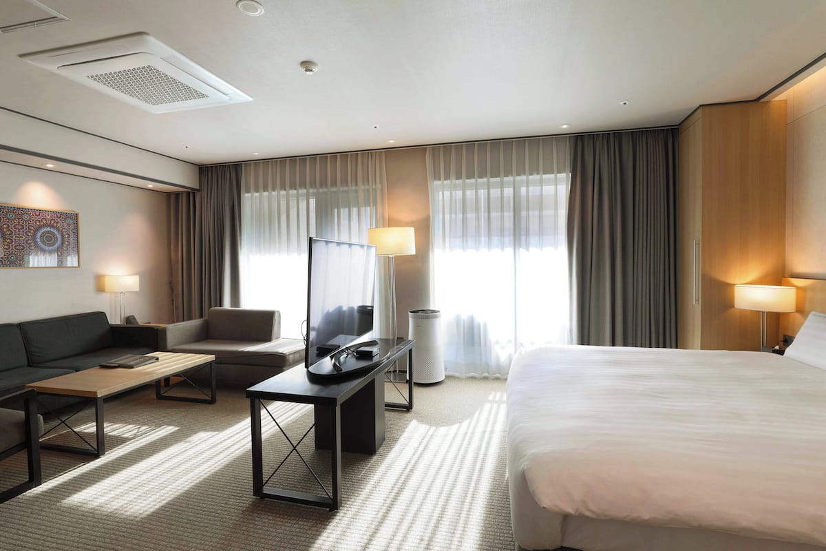 Une chambre d’hôtel avec un lit, un canapé, un bureau, une télévision et une lampe.