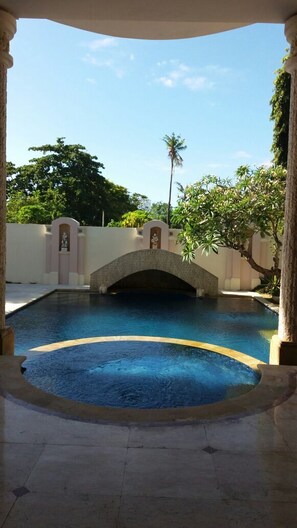 Piscina com uma ponte de pedra, rodeada por muros e árvores.
