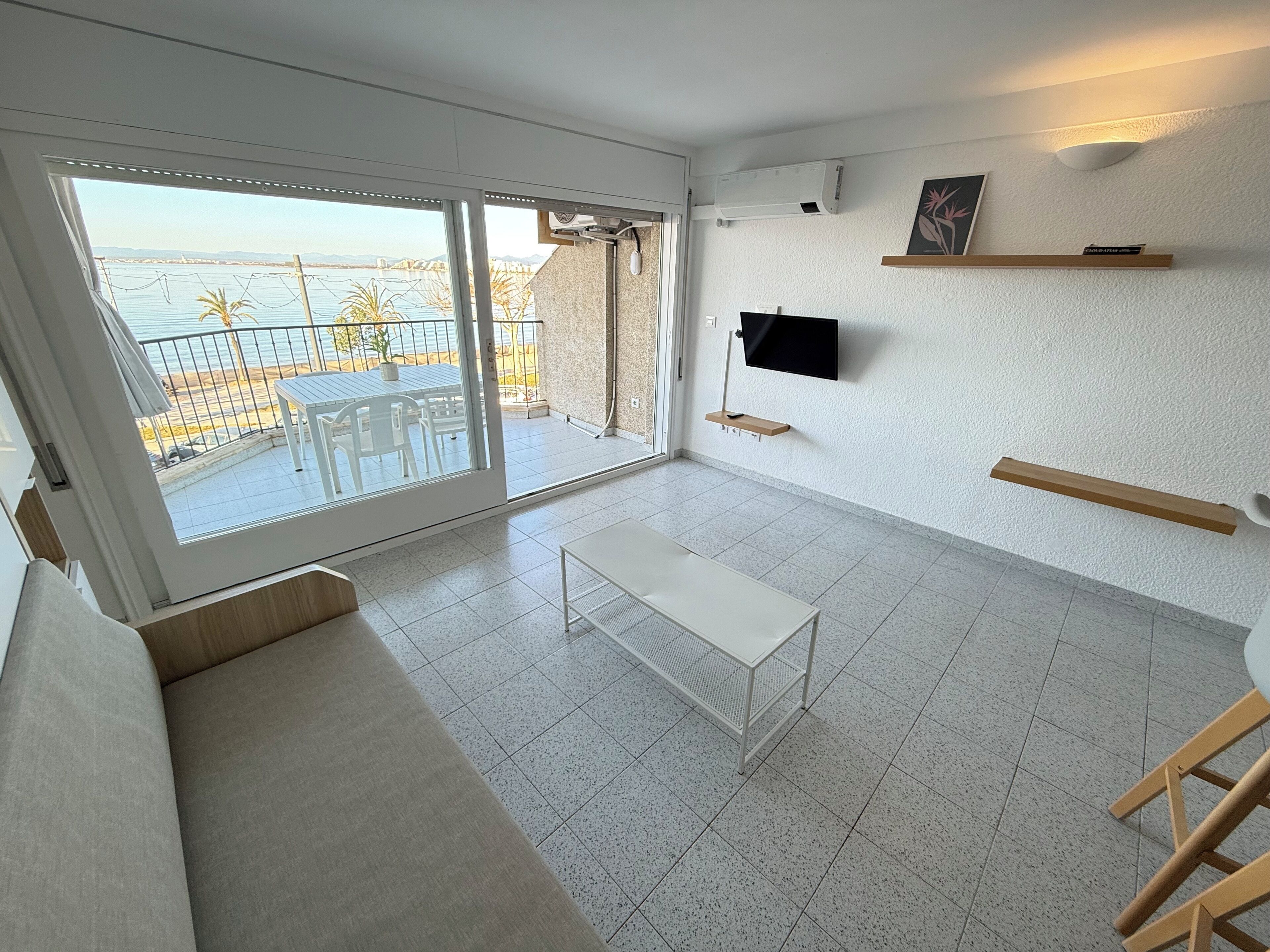 Une chambre moderne dotée d’une grande porte-fenêtre coulissante qui donne sur un balcon offrant une vue sur la mer. On y trouve une table blanche et un banc.