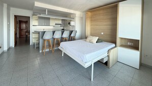 A modern bedroom with a bed, a wooden wardrobe, and a kitchenette area with bar stools. - Agi Pi Sunyer 4 2B Apartamento for rent in Roses Girona. (Rosas / Roses)