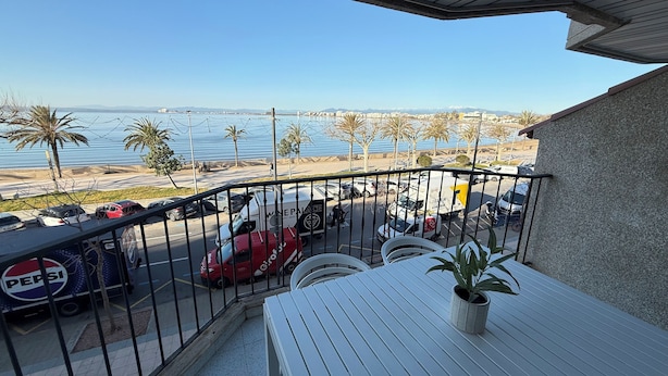 A balcony with a view of the sea, parked cars, and a Pepsi truck. - Agi Pi Sunyer 4 2B Apartamento for rent in Roses Girona. (Rosas / Roses)