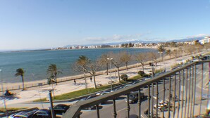 A coastal cityscape with a view of the sea, a beach with palm trees, and a road with cars. - Agi Pi Sunyer 4 2B Apartamento for rent in Roses Girona. (Rosas / Roses)