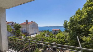 A balcony with a view of the sea, a garden, and a building with a red roof.