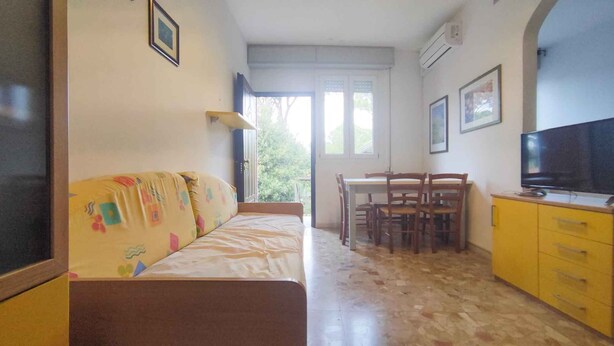 A small, cozy room with a sofa, a dining table with chairs, a TV, and a yellow cabinet.